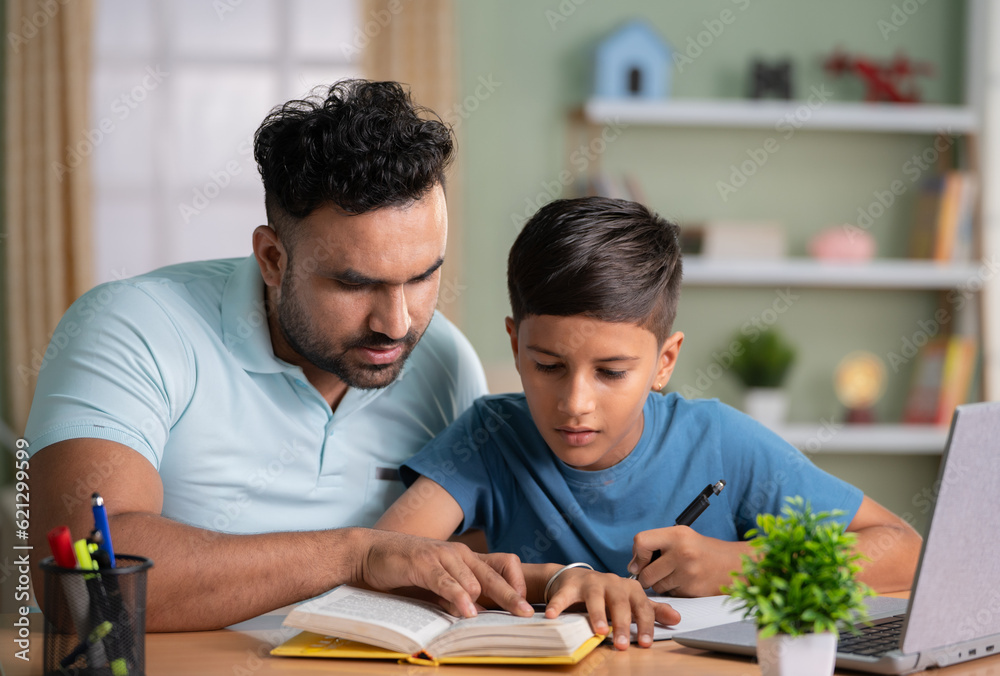 Indian father teaching or helping the son for reading from book at home - concept of Parental Guidance, home education and Tutoring Sessions. - obrazy, fototapety, plakaty 