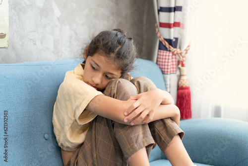 Photo Portrait Of Upset Little Girl Sitting On Couch At Home, Depressed Preteen Female