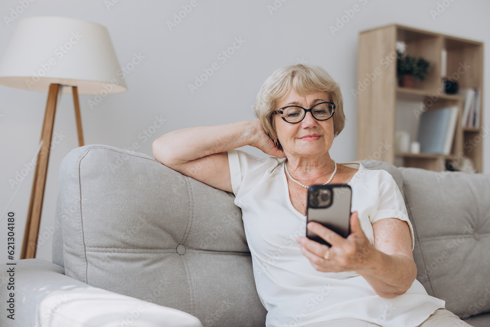 Senior woman with mobile phone on her hands sitting in room and sending messages to her friends and family. Senior woman typing on her mobile phone Senior woman with mobile phone on her hands sitting in room and sending messages to her friends and family. Senior woman typing on her mobile phone