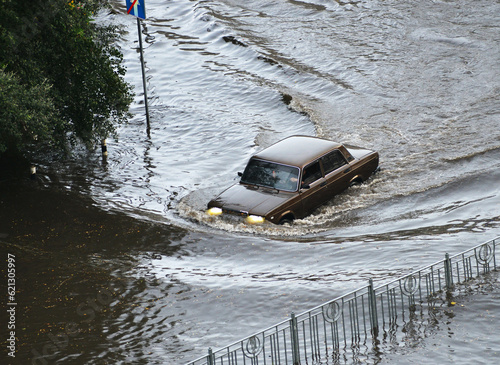 Kyiv, Ukraine - July 7, 2023: A brown car passes through a flooded road area after heavy rain