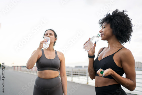 Drink water from a bottle Break athletes friends women rest . Friends workout fitness running in sportswear.