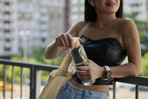 Young Asian female opening a glass bottle of mineral water. Unrecognizable Southeast Asian woman taking off a bottle cap to drink filtered water