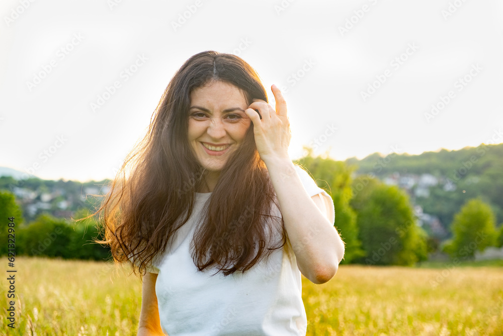 Happy 30-year-old woman straightening her hair in the wind while walking in nature in the field in summer Happy 30-year-old woman straightening her hair in the wind while walking in nature in the field in summer