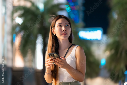 Asian woman using a smartphone standing against Bangkok city walking street at night