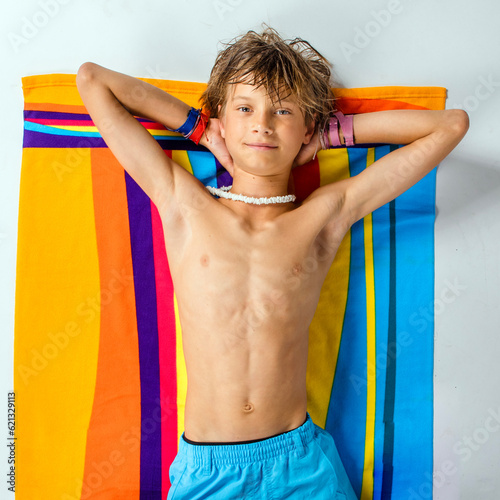 Smiling confident preteen boy lying back shirtless relaxing on his colorful beach towel