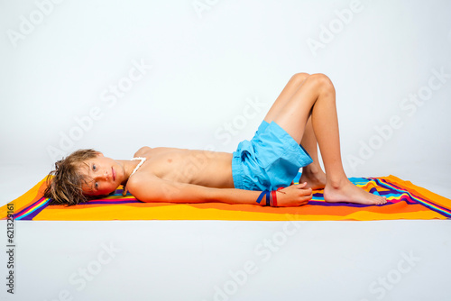 Φωτογραφία Young shirtless preteen boy in swim trunks lying down on a colorful beach towel