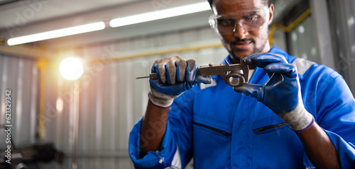 Professional black male engineer or Technician, Worker examining using vernier caliper measure of a workpiece steel for checking size in a workshop machine factory.