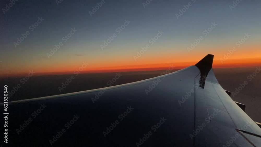 The view from an airplane window over the wing to a beautiful orange and blue sunset in the evening. The view from an airplane window over the wing to a beautiful orange and blue sunset in the evening.