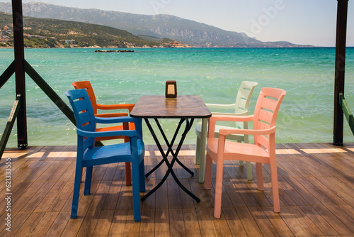 Empty table with four colorful chairs  on the pier above the turquoise sea