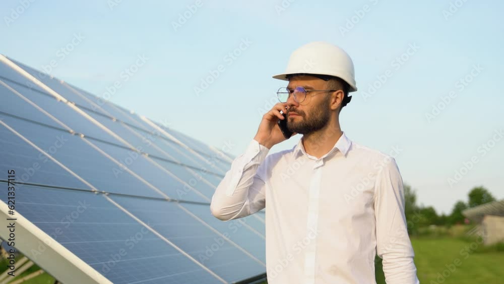 Confident engineer wearing safety hard hat, holding mobile phone, making a call and walking. Engineer, worker, or architect working with Solar panel concept Confident engineer wearing safety hard hat, holding mobile phone, making a call and walking. Engineer, worker, or architect working with Solar panel concept