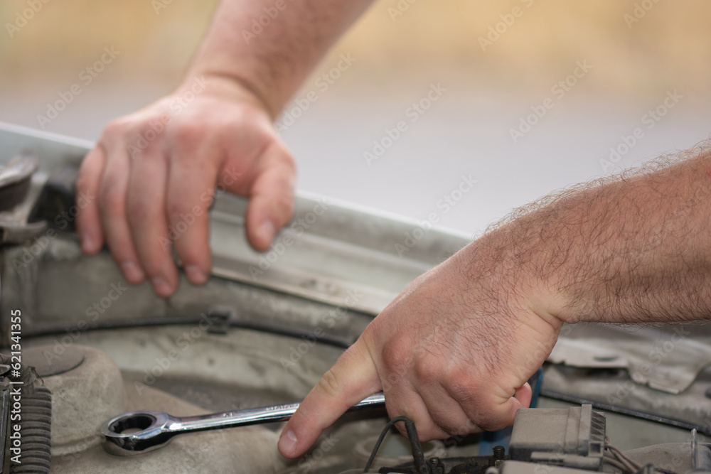 repairing a car, the hands of a mechanic tigheten a nut with a metal wrench repairing a car, the hands of a mechanic tigheten a nut with a metal wrench