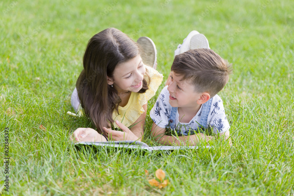 Two children reading a book together on the grass in the park. Two children reading a book together on the grass in the park.