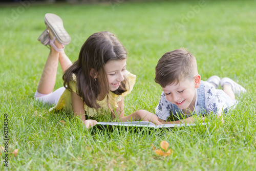 Cute little children lying on the grass reading a book