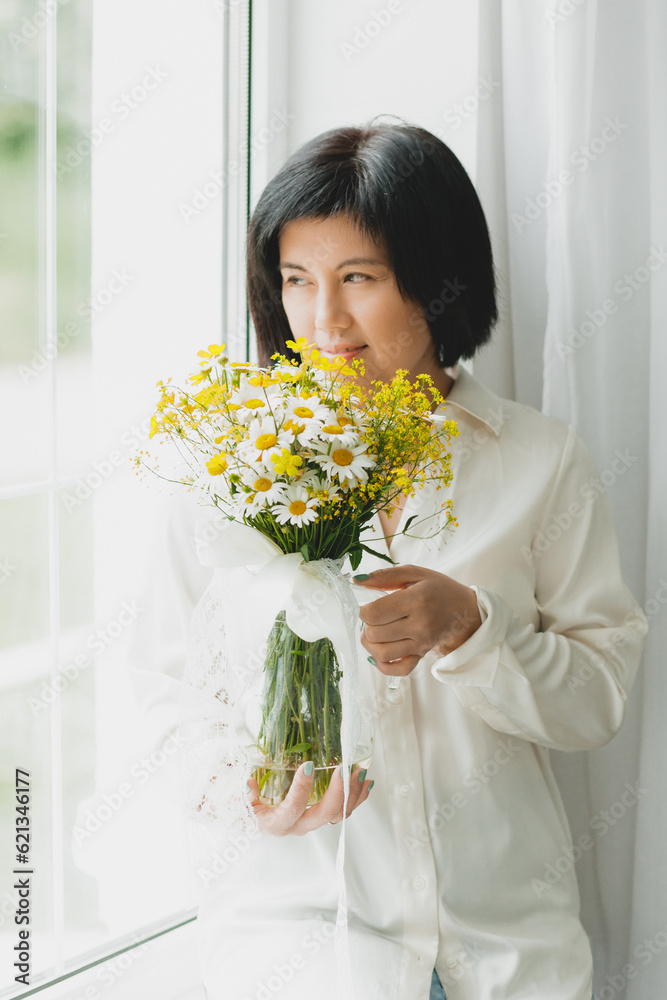 portrait of an asian woman with a bouquet of wild flowers at home near the window. portrait of an asian woman with a bouquet of wild flowers at home near the window.