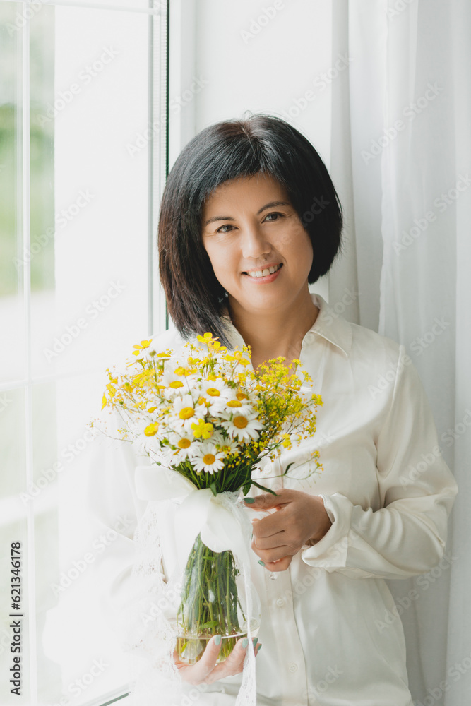 portrait of an asian woman with a bouquet of wild flowers at home near the window. portrait of an asian woman with a bouquet of wild flowers at home near the window.
