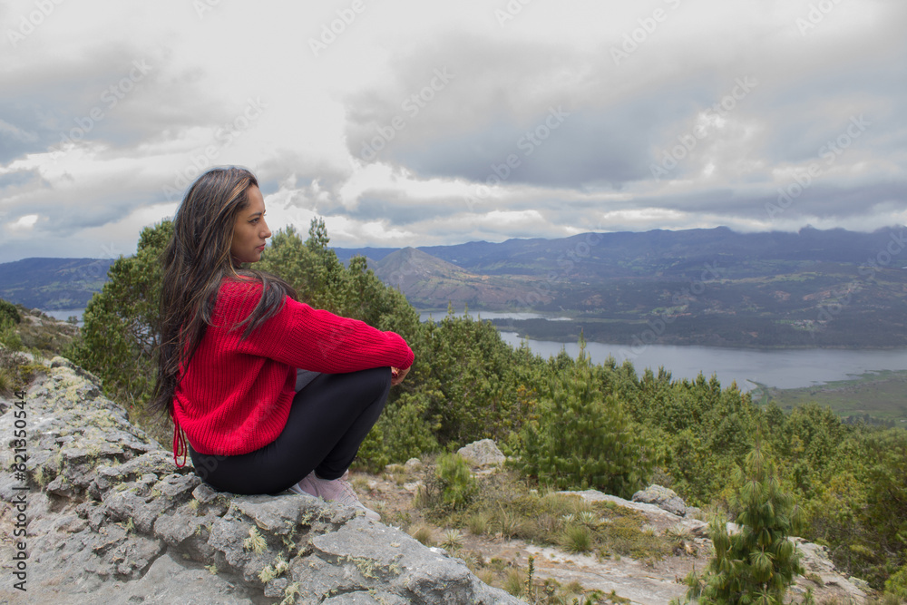 lonely woman sitting on a mountain looking at the landscape and a lake