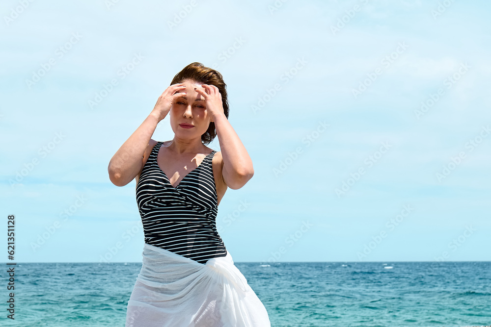 Pretty sexy woman in swimsuit and white pareo enjoying sunny windy day near blue sea. Happy female enjoying the life. Beach summer, travel concept. Pretty sexy woman in swimsuit and white pareo enjoying sunny windy day near blue sea. Happy female enjoying the life. Beach summer, travel concept.
