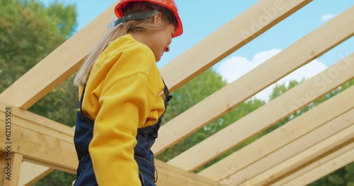 smiling cheerful young woman in hardset uniform having fun laughing while male colleague working in construction site, girl holding drill looking at camera in unfinished building house cottage site photo