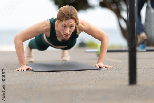Adult athletic woman with no make up doing push ups outdoors