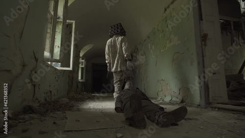 Ghost of maniac with cage on his head dragging dead body down corridor of asylum