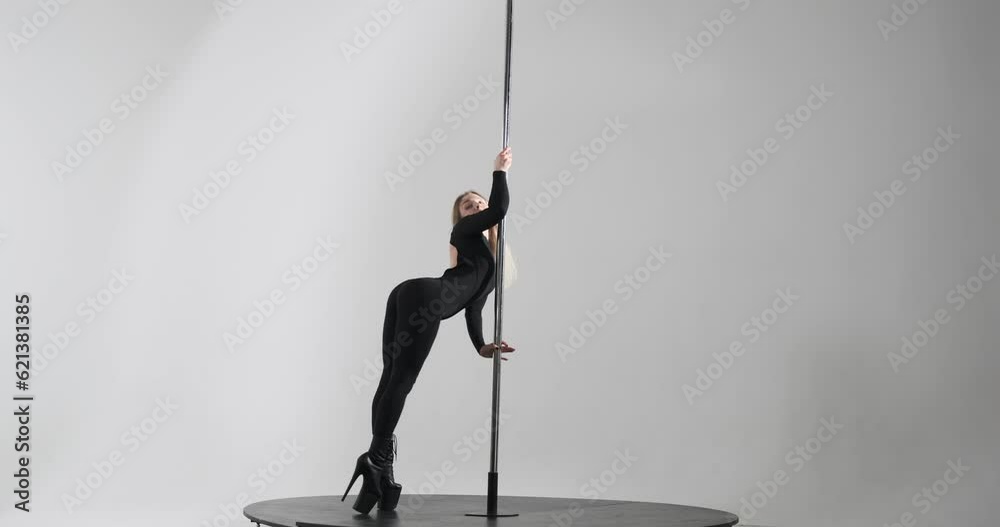 Caucasian dancer captivates with seductive pole dance. Dressed in a sleek black dance bodysuit and high heels, she effortlessly moves around the pole, showcasing her grace, strength, and flexibility