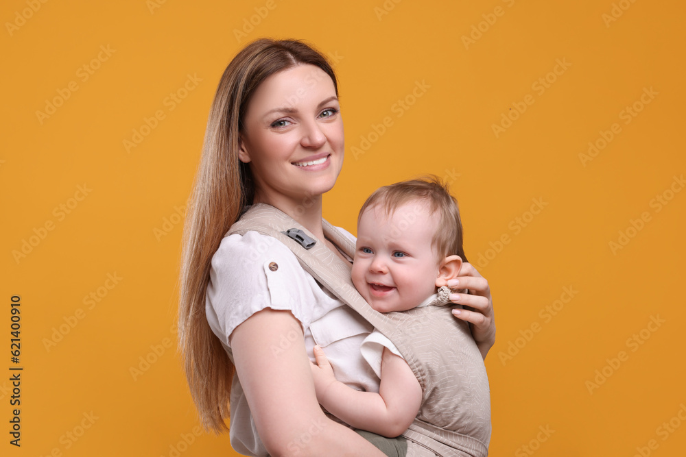 Mother holding her child in sling (baby carrier) on orange background