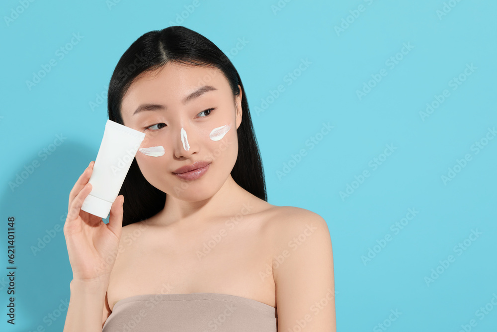 Beautiful young woman with sunscreen on her face holding sun protection cream against light blue background, space for text Beautiful young woman with sunscreen on her face holding sun protection cream against light blue background, space for text