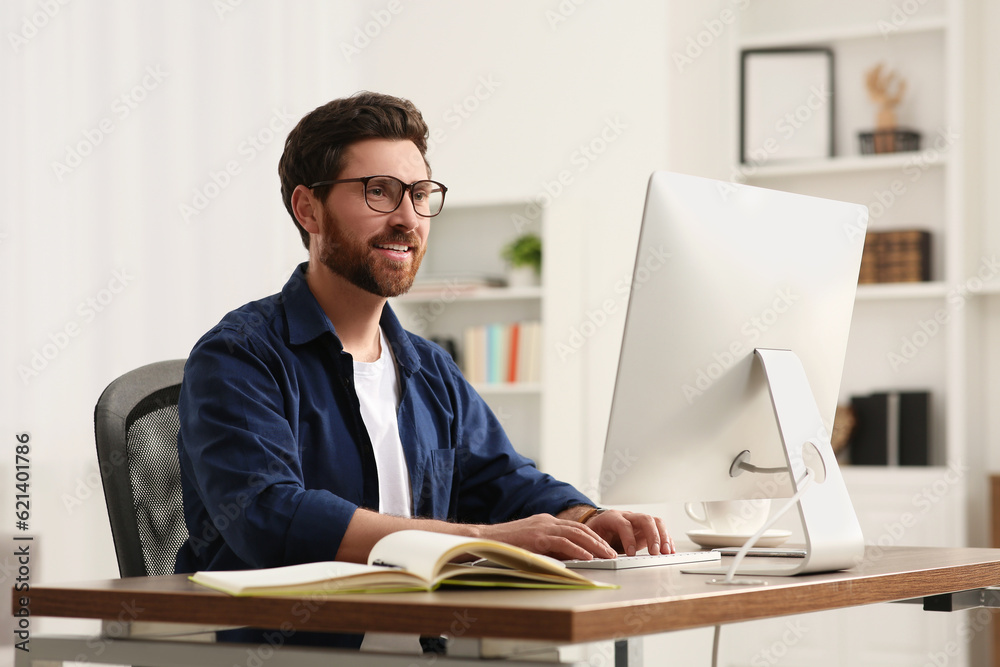 Home workplace. Happy man working with computer at wooden desk in room Home workplace. Happy man working with computer at wooden desk in room