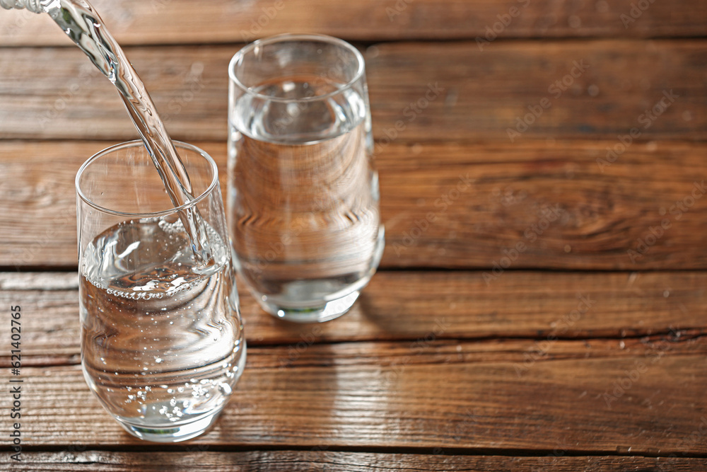 Pouring water into glass on wooden table, space for text Pouring water into glass on wooden table, space for text
