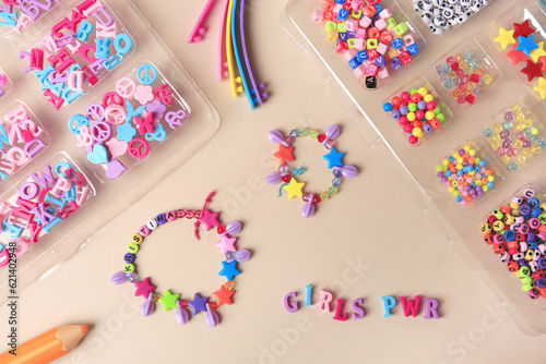 Handmade jewelry kit for kids. Colorful beads, wristbands and bracelets on beige background, flat lay