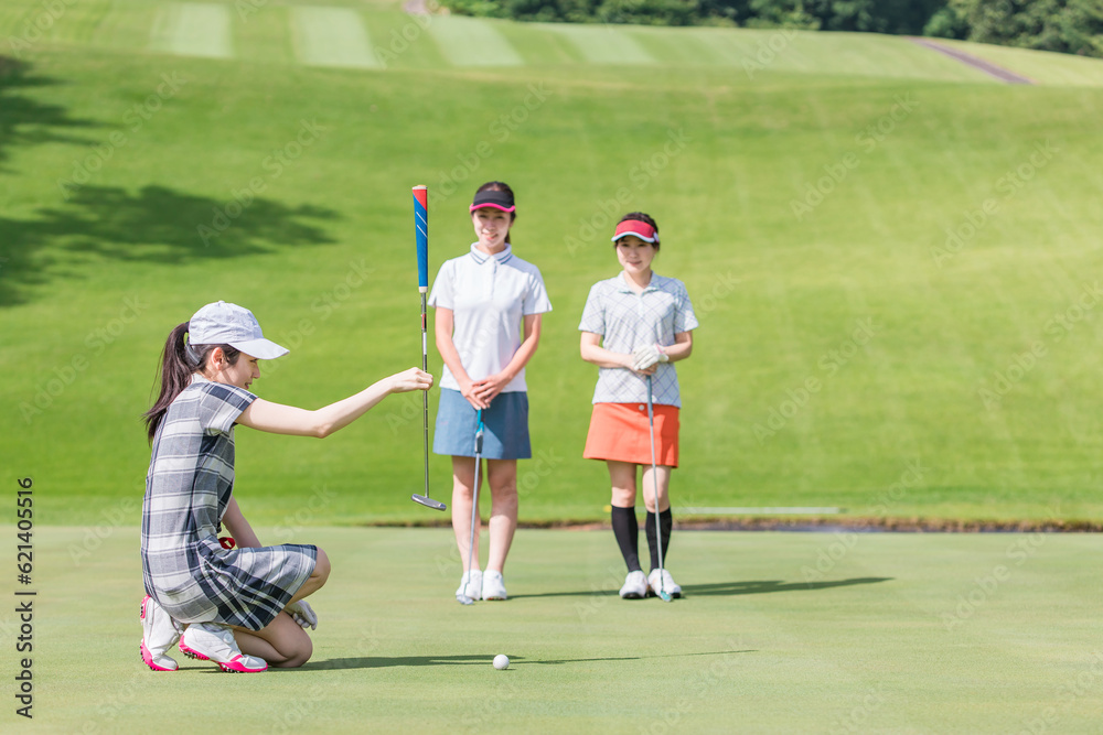 Obraz premium ゴルフ場のグリーンでゴルフをするゴルファーの女性(パター) 