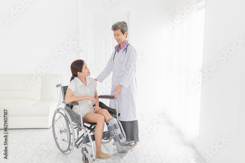 Asian patient sitting on wheelchair, patient wear air cast walking boot, doctor and patient talk about symptoms and treatment plan, rehabilitation activity