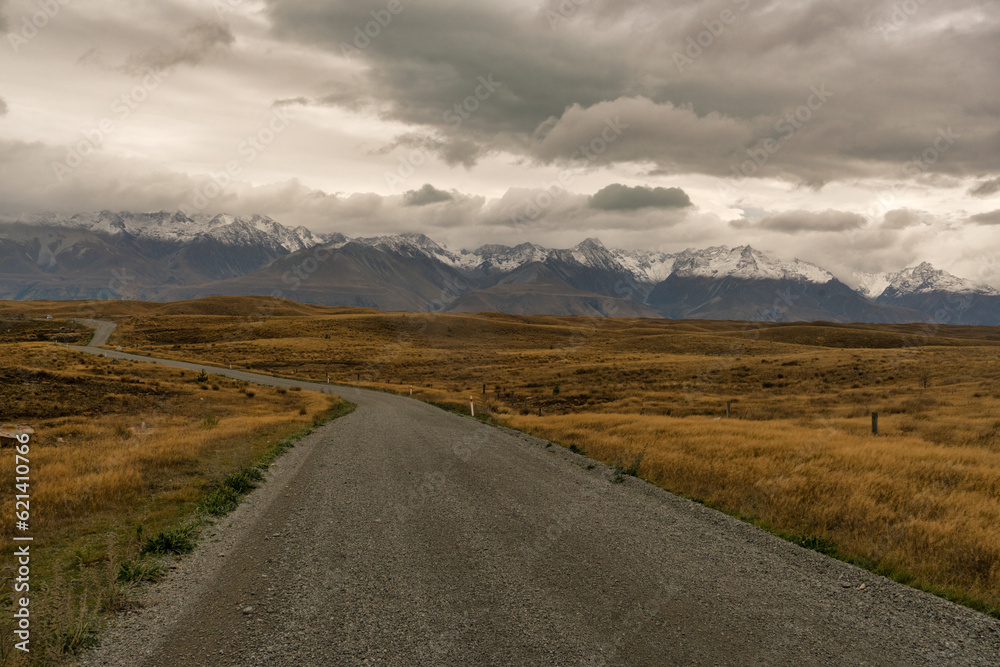Driving towards the snow covered Southern alps on a windy gravel road through rural farmland  between Lake Takapo and Lake Pukaki