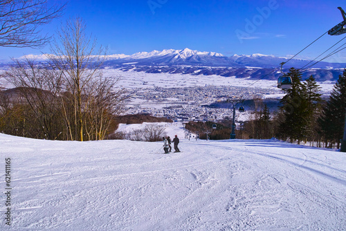 快晴の富良野スキー場から見る大雪山と十勝岳連峰、北の峰ゾーンのゴンドラリフト横の中級者コース上部で休息しゲレンを眺める三人のスキーヤー達
 photo