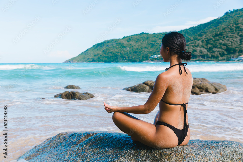 Harnessing the vibrant energy of the beach, a joyful woman in a bikini recharges her body and soul through yoga, feeling invigorated and alive.