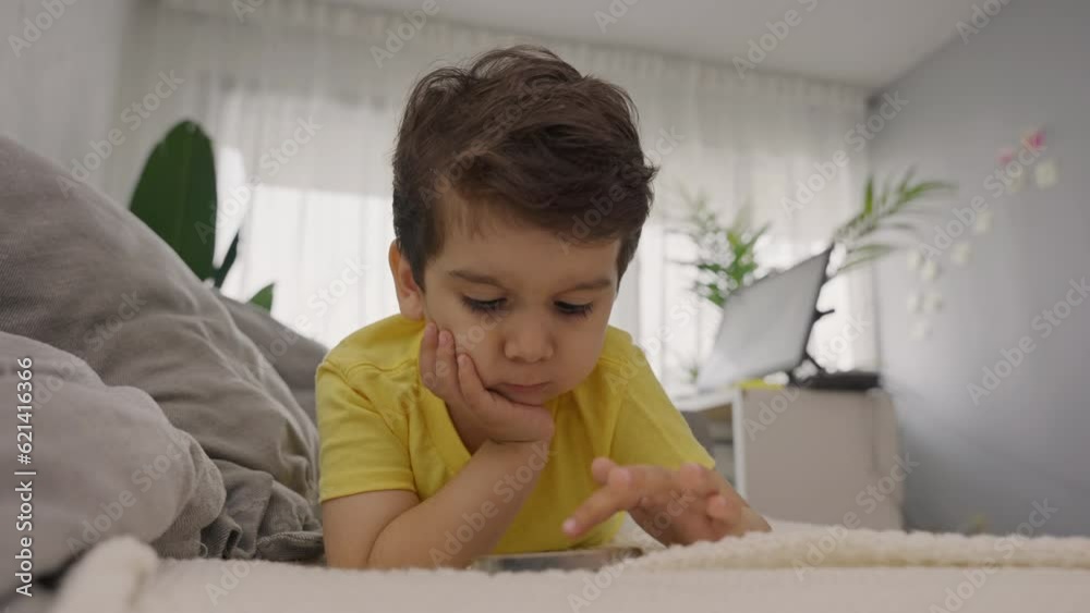 Adorable little child lying on sofa touching mobile phone screen Adorable little child lying on sofa touching mobile phone screen