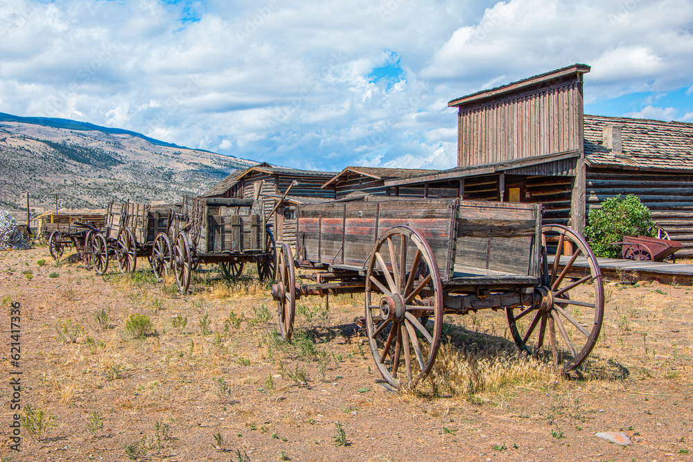 Historic wagons and buildings with mountains, blue sky, and clouds. Wyoming, USA