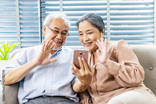 Fototapeta Naklejka Na Ścianę i Meble -  Happy elderly retired couple making video call with mobile phone, gesturing hi, having pleasant conversation,chatting with grown up children grandchildren using wireless internet connection at home