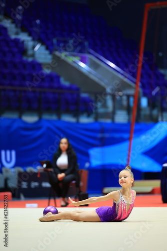 gymnastics and ball between legs of performance, competition training or dancing in dark sports arena. Female athlete, rhythmic movement and creative talent in solo concert, agility or balance