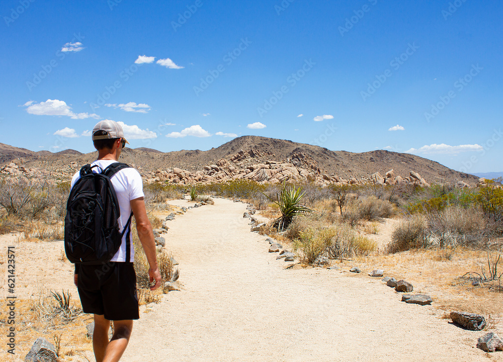 Close up of the young man walking the trail road toward rocky montains on Arch Rock Trail in Joshua Tree National Park, California