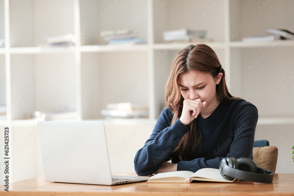 Stressed, A beautiful caucasian female student is studying remotely. She is sitting at a table at home with a laptop and a notepad and concentrated is watching a video conference lesson. Stressed, A beautiful caucasian female student is studying remotely. She is sitting at a table at home with a laptop and a notepad and concentrated is watching a video conference lesson.