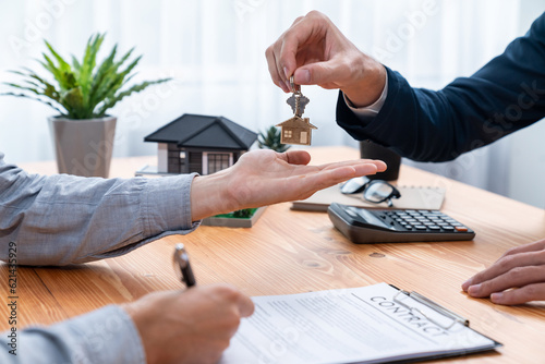 Real estate agent handing house key to buyer after signing rental least contract during house loan meeting. Successful property sale purchase agreement for new home ownership. Entity photo