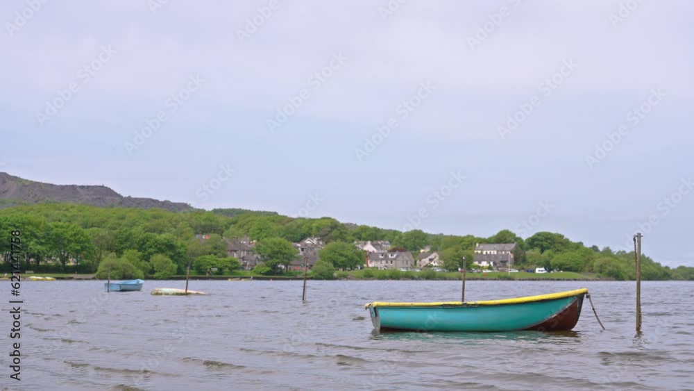 Wide shot of lone multicolor boat on the waves of Lake Llyn Padarn on a spring day in the village Llanberis, Wales, UK Wide shot of lone multicolor boat on the waves of Lake Llyn Padarn on a spring day in the village Llanberis, Wales, UK