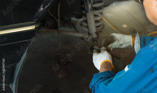 Close-up of a mechanic inspecting a car's suspension bush while comparing damage, replacing parts, and raising the vehicle in a garage.