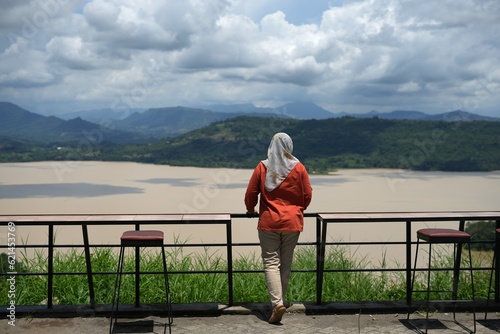 A woman wearing a hijab is in front of the lake enjoying the view