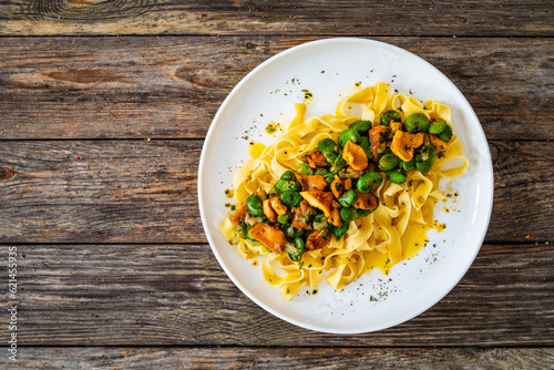 Tagliatelle with broad bean and chanterelle mushrooms on wooden table 