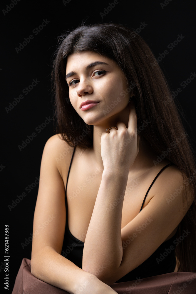 Classic studio portrait of a young brunette dressed in a black top, who is sitting on a chair against a black background. Classic studio portrait of a young brunette dressed in a black top, who is sitting on a chair against a black background.