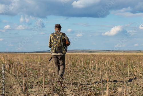 Mature man hunter with gun while walking on field. © Budjak Studio