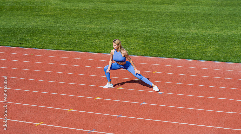 Fototapeta premium Sports exercises and stretching in the stadium. Physical training girl. Fit girl do outward lunging. Physical training education. Sports lesson. Female runner stretching before workout