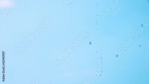 Raindrops falling on the transparent glass on a blue background give a feeling of coldness and loneliness.
